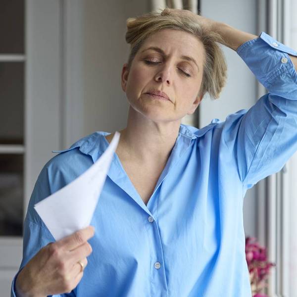 Menopausal Mature Woman Having Hot Flash At Home Cooling Herself With Letters