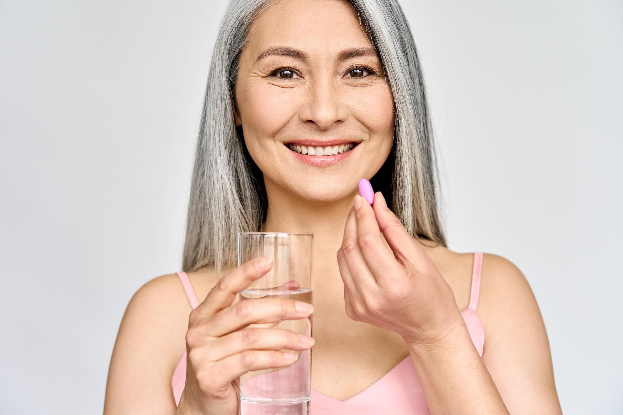 middle aged 50s Asian woman holding pill and glass of water
