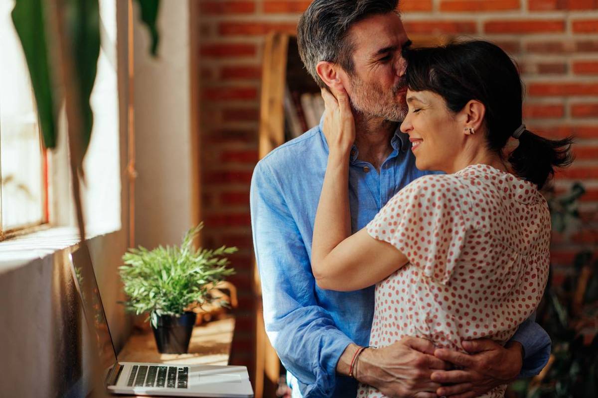 middle-aged man kissing his wife on the forehead while she enjoying in his hug