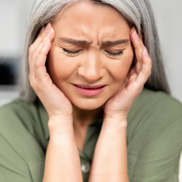 Middle-aged woman with long silver hair rubbing temples, suffering from migraine