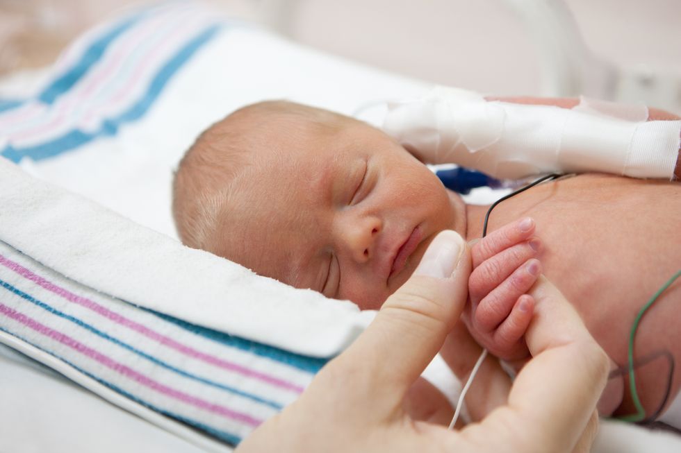 mother holdind hand of a premature baby in incubator