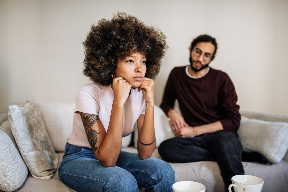 Multi ethnic couple in living room drinking coffee or tea and expressing negative emotions