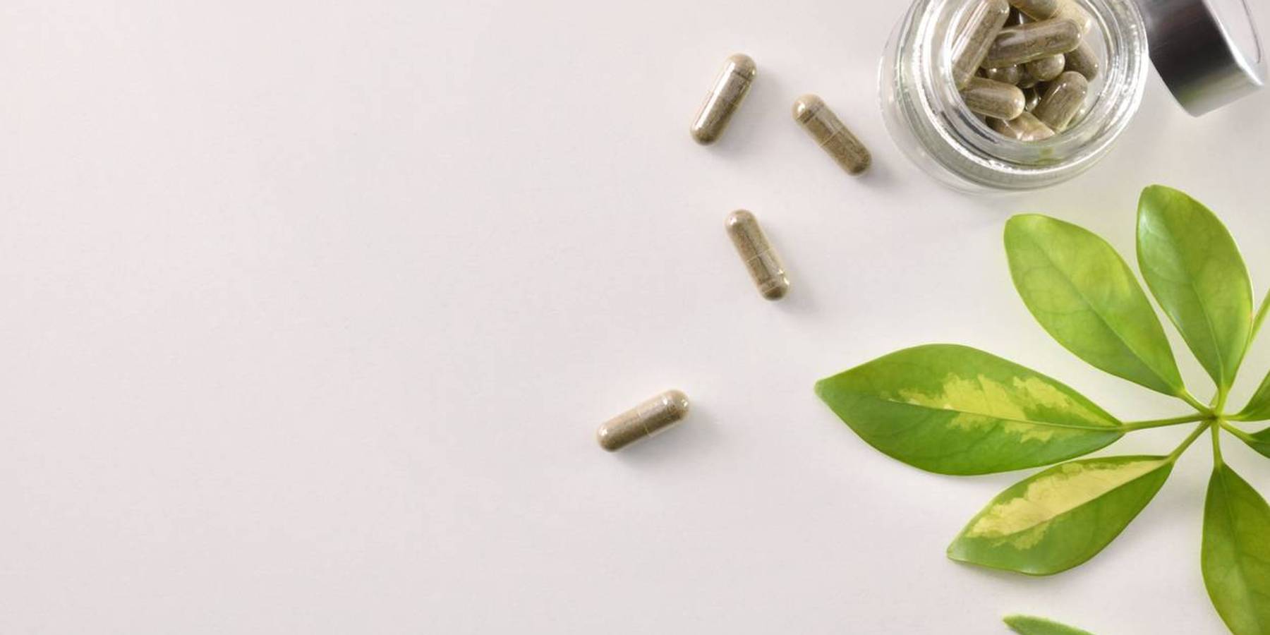 Natural medicine capsules in open glass jar on table