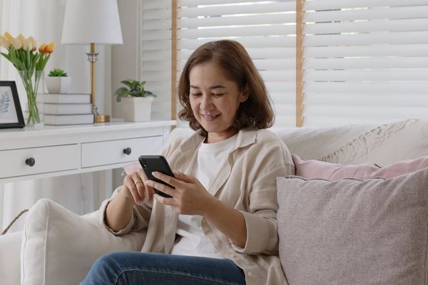 Older adult asia female sit relax on sofa couch smiling while looking at her smartphone