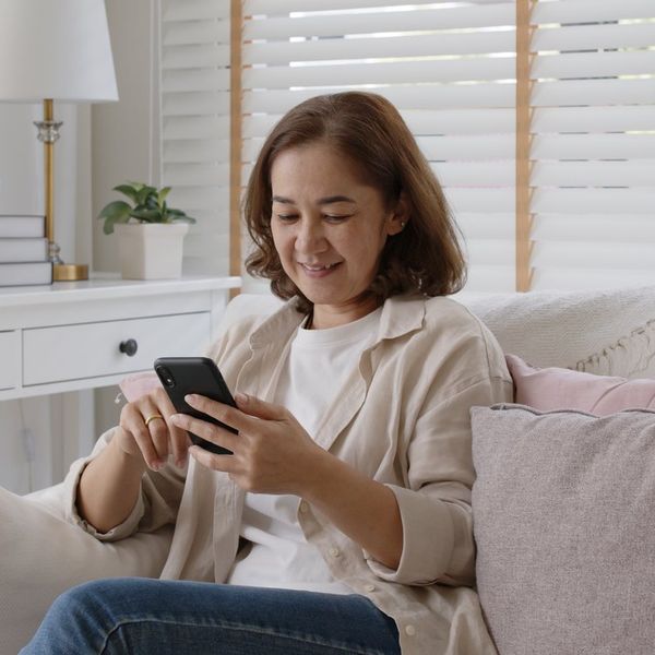 Older adult asia female sit relax on sofa couch smiling while looking at her smartphone