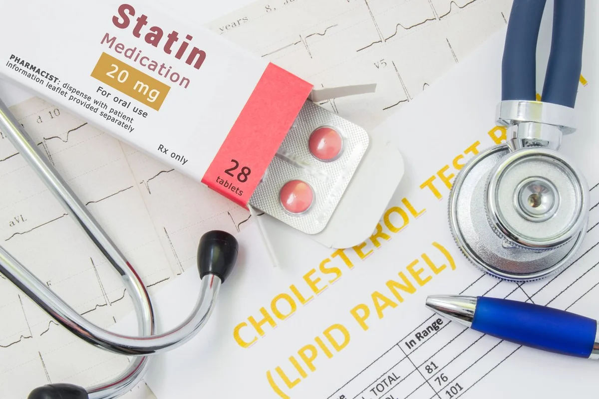 Open packaging with drugs tablets, on which is written "Statin Medication", lies near stethoscope, result analysis on cholesterol (lipid panel) and ECG