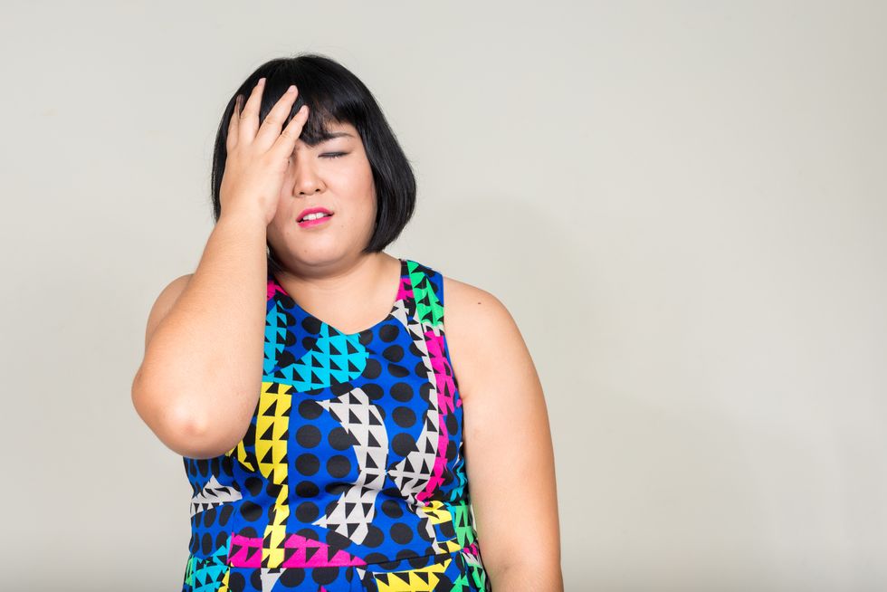 overweight Asian woman looking stressed and holding hand on her head while having eyes closed