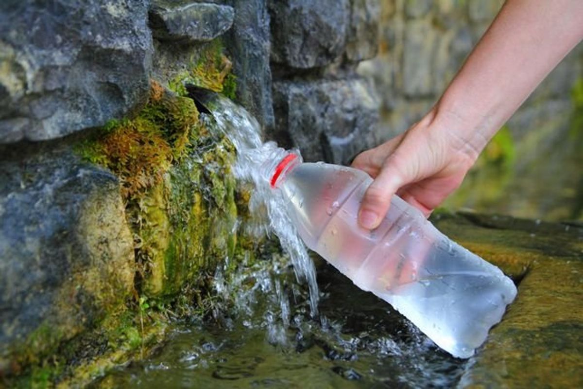 person filling a water bottle in a stream