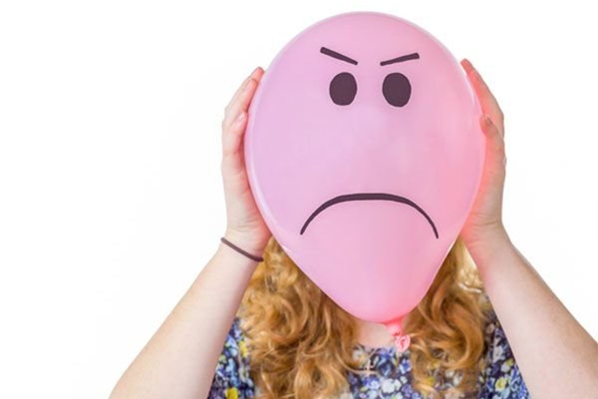 person holding a balloon with a sad face drawn on it