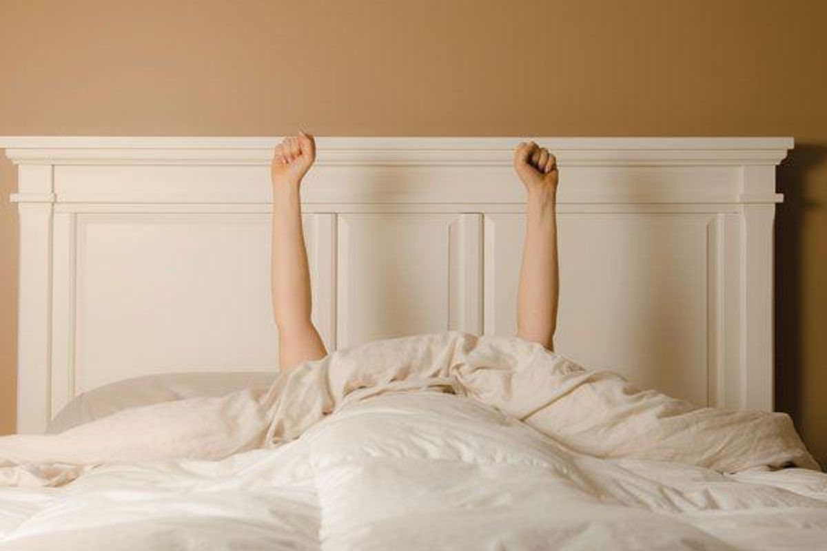 person in bed holding their arms up