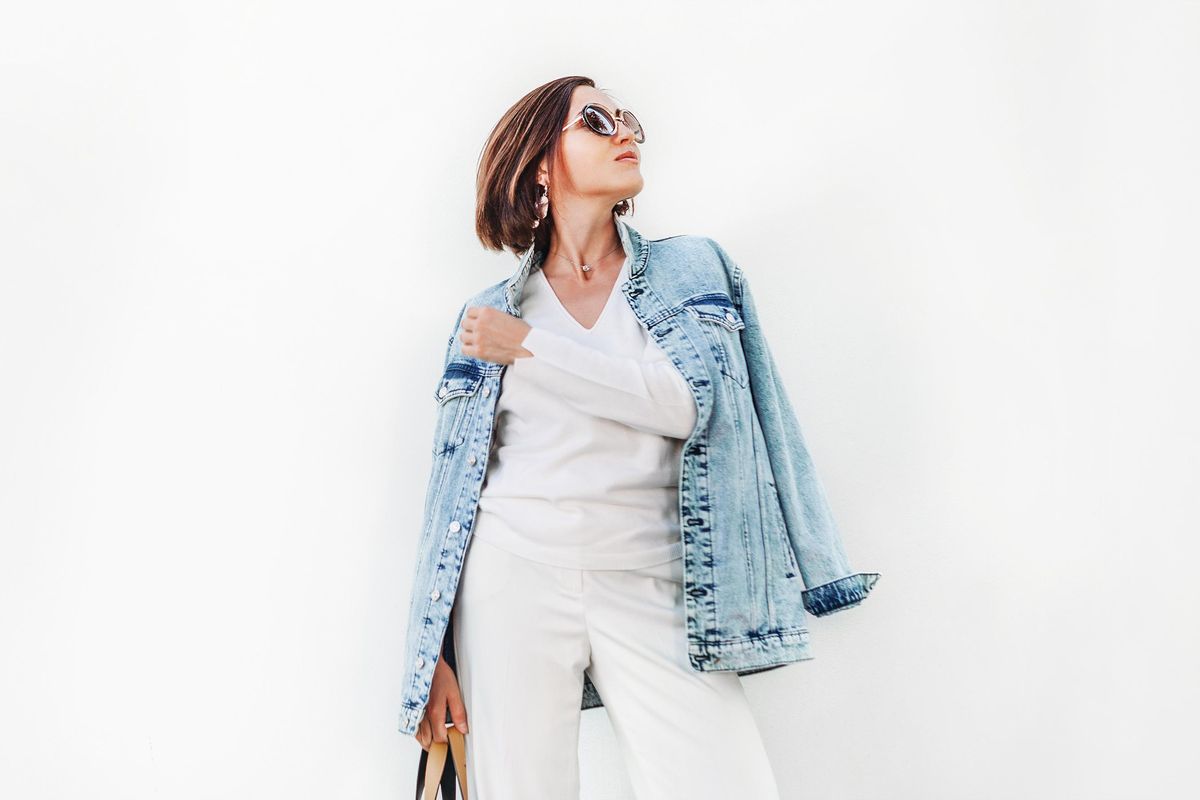 Posing woman in elegant white outfit with oversize denim jacket