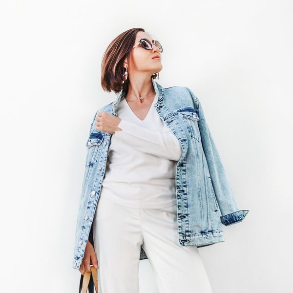 Posing woman in elegant white outfit with oversize denim jacket
