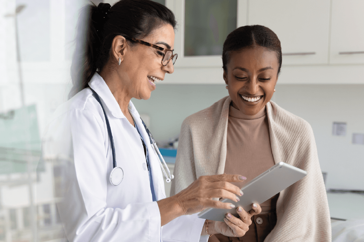 practitioner woman and cheerful young African patient woman watching examination medical report on tablet