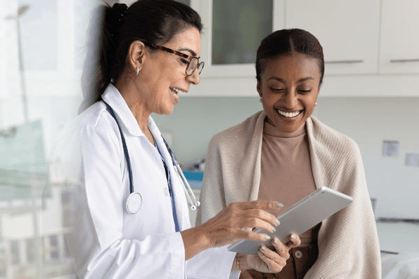 practitioner woman and cheerful young African patient woman watching examination medical report on tablet