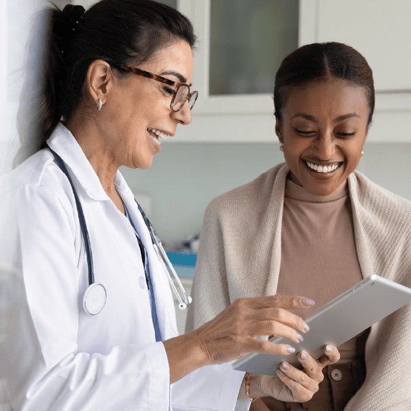 practitioner woman and cheerful young African patient woman watching examination medical report on tablet