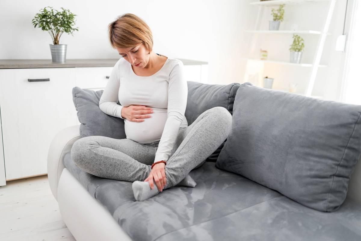 Pregnant tired exhausted woman with stomach, leg and pain issues at home on a couch