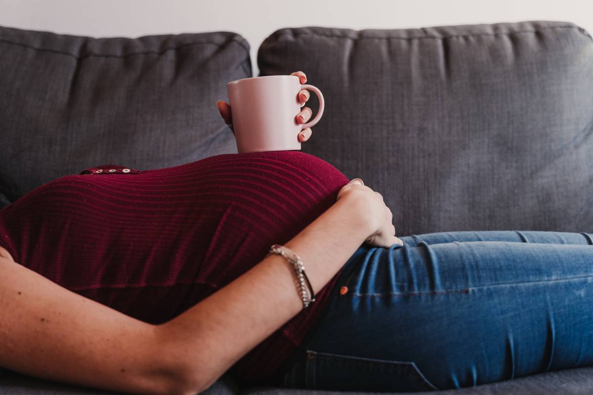 pregnant woman at home lying on the sofa and holding a cup on belly