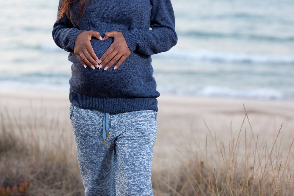 Pregnant woman doing heart shape with hand on her belly.