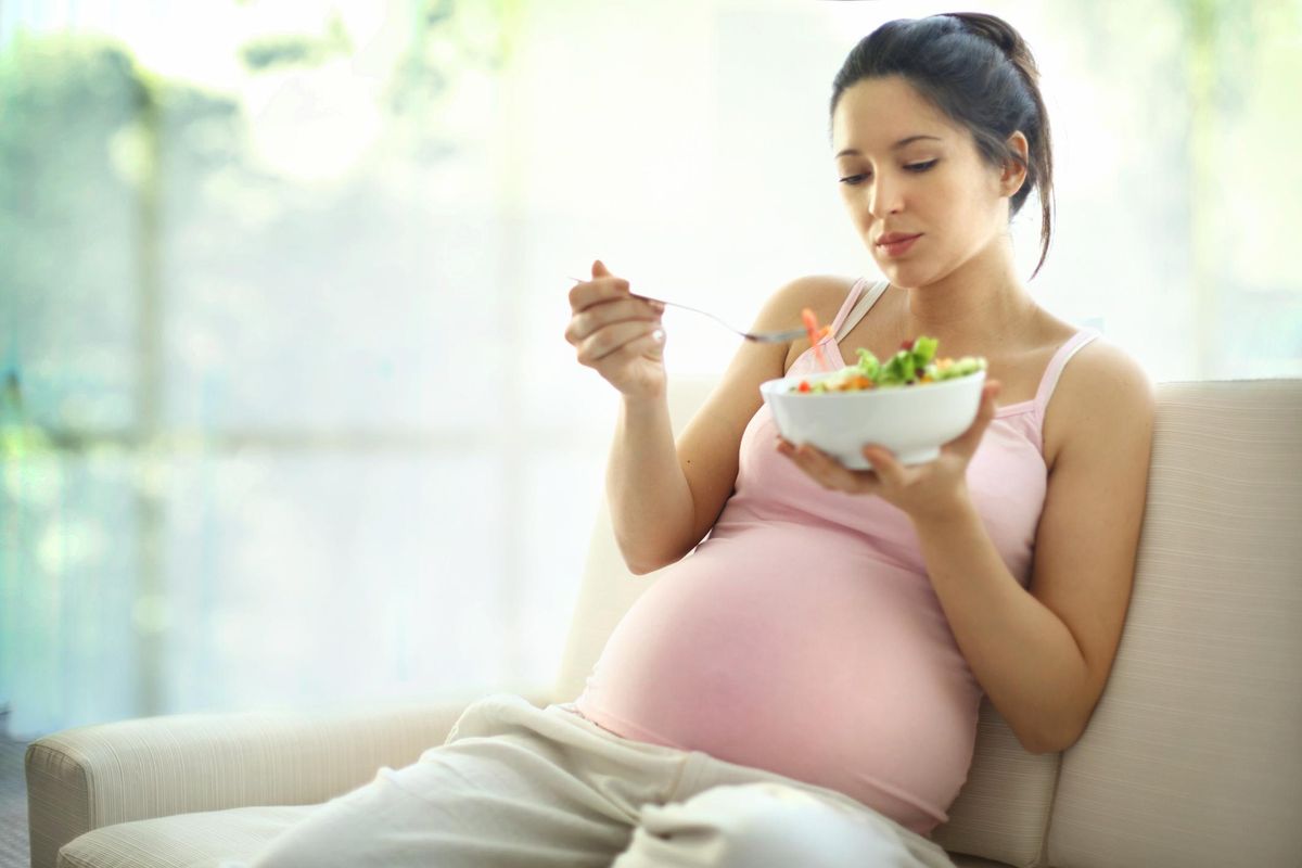 pregnant woman eating a bowl of salad