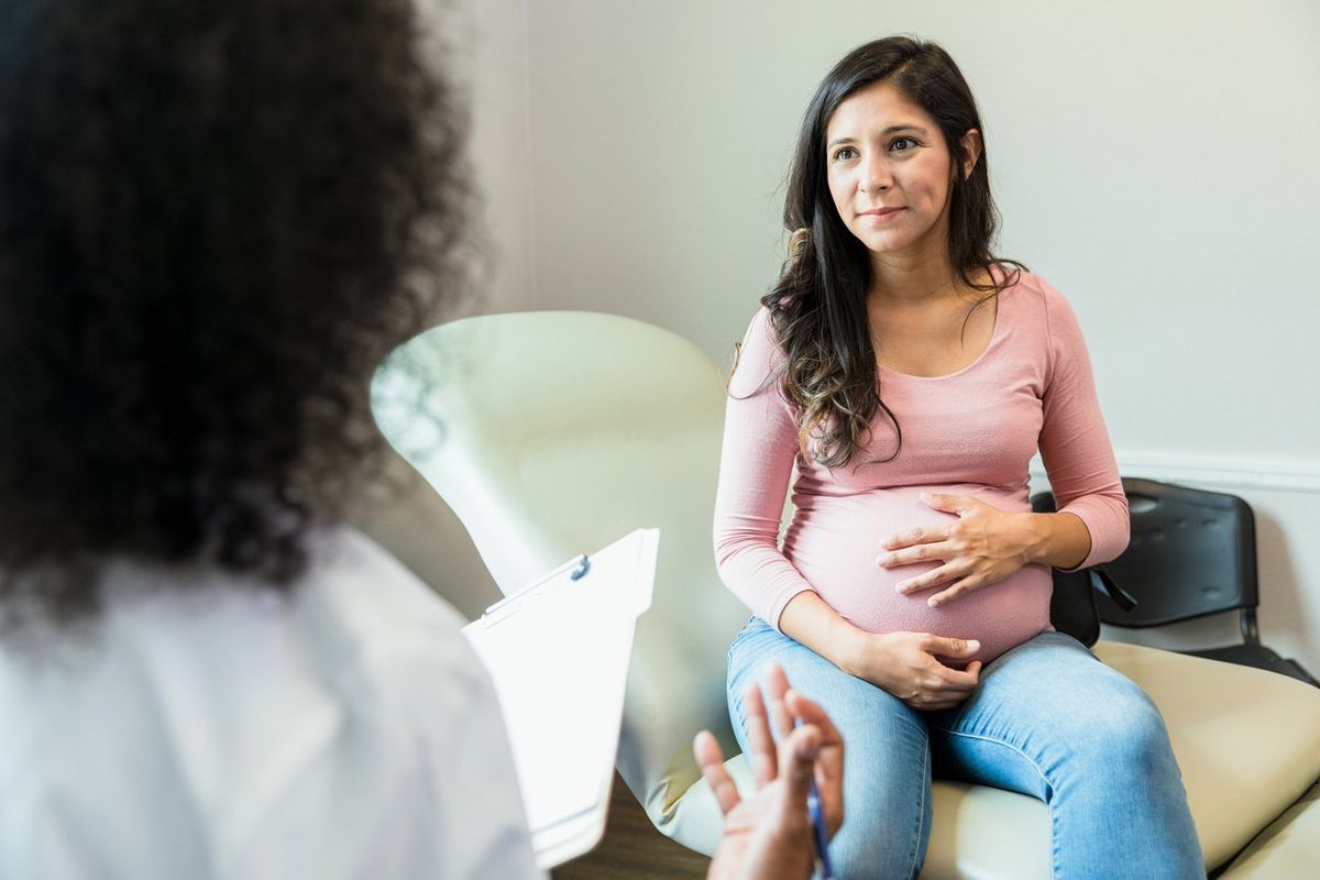 pregnant woman touches her abdomen as she listens to the unrecognizable female doctor.