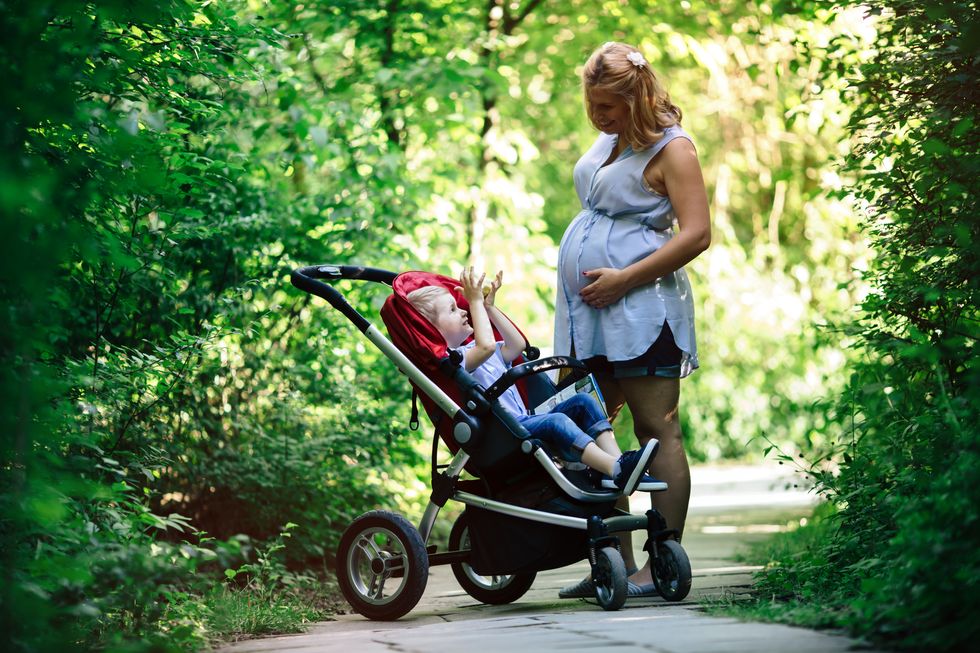 Pregnant woman with her child in pram walking in nature