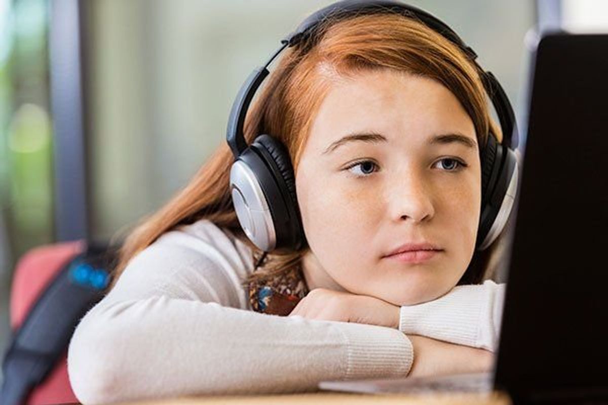 preteen girl listening to headphones while using laptop