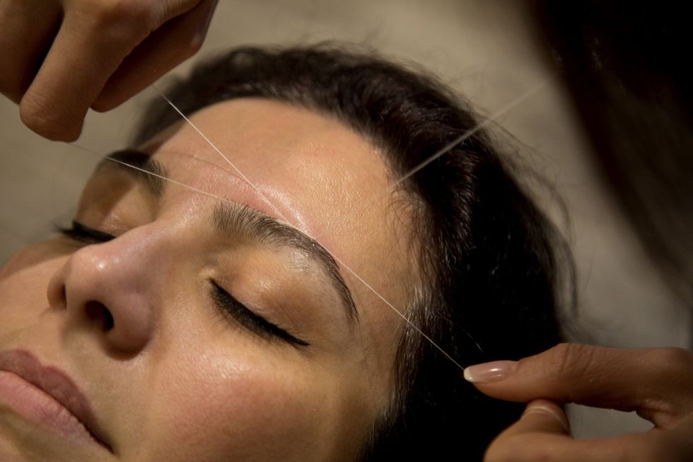 Professional eyebrow hair removal service on a woman in a hair salon.