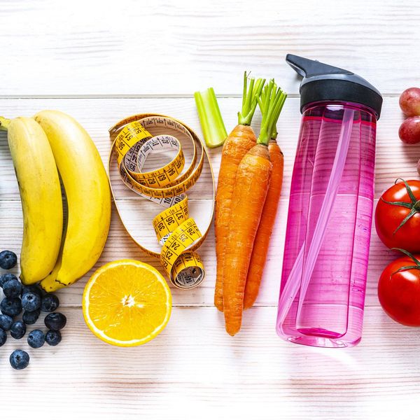 rainbow colored dumbbells, jump rope, water bottle, towel, tape measure and healthy fresh organic vegetables, fruits and nuts arranged side by side