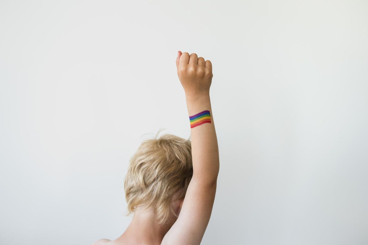 Raised child hand with rainbow LGBTQ pride flag tattoo. Movement symbol