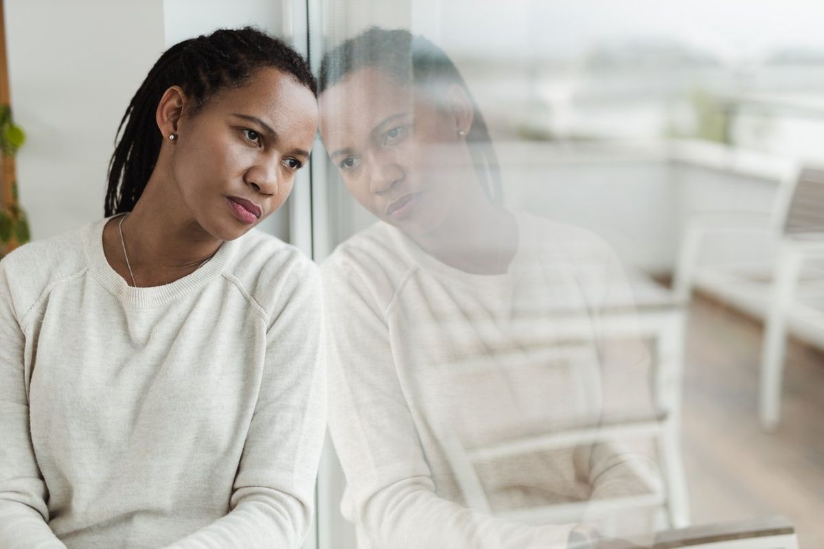 Sad African American woman looking through window from home