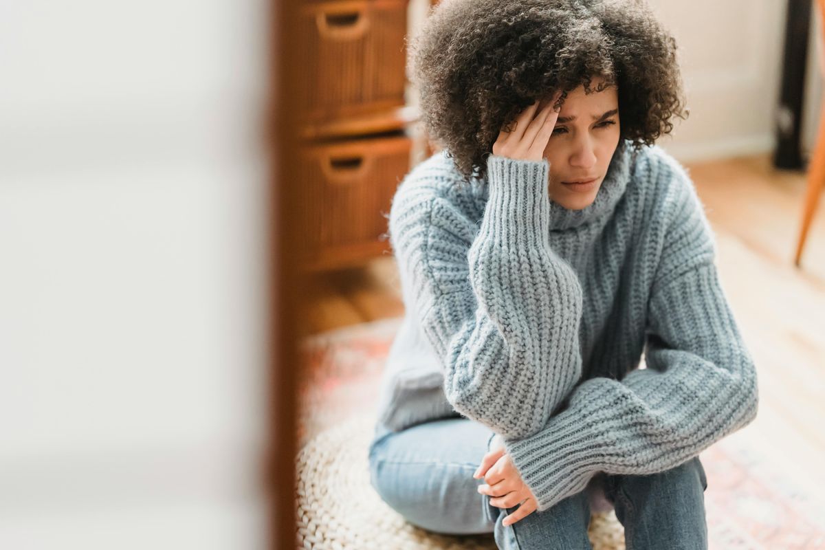 Sad ethnic woman crying on pouf in apartment