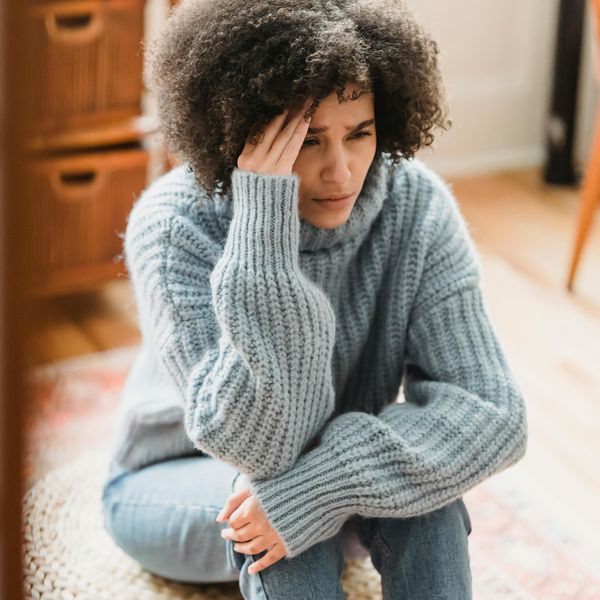 Sad ethnic woman crying on pouf in apartment