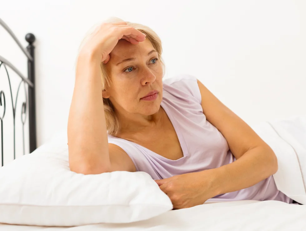 Sad middle-aged female with head reclined upon hands in bed