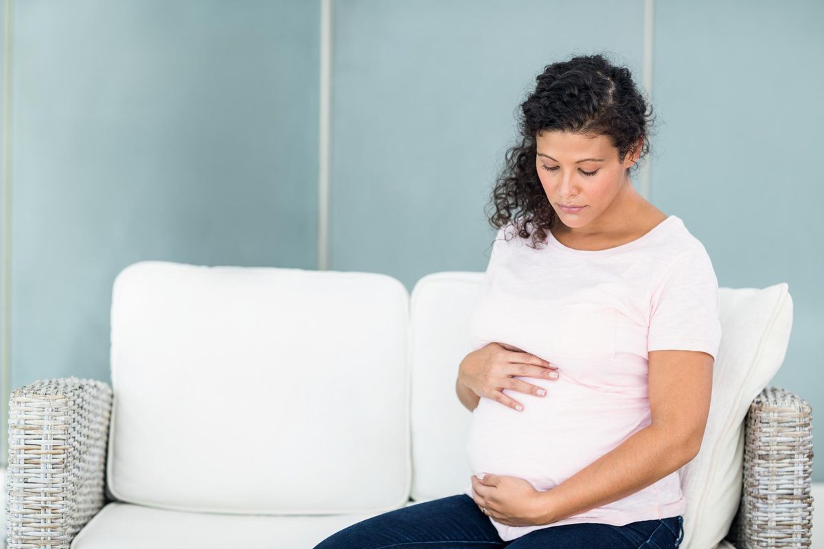 Sad pregnant woman addicted to opioids sitting on sofa