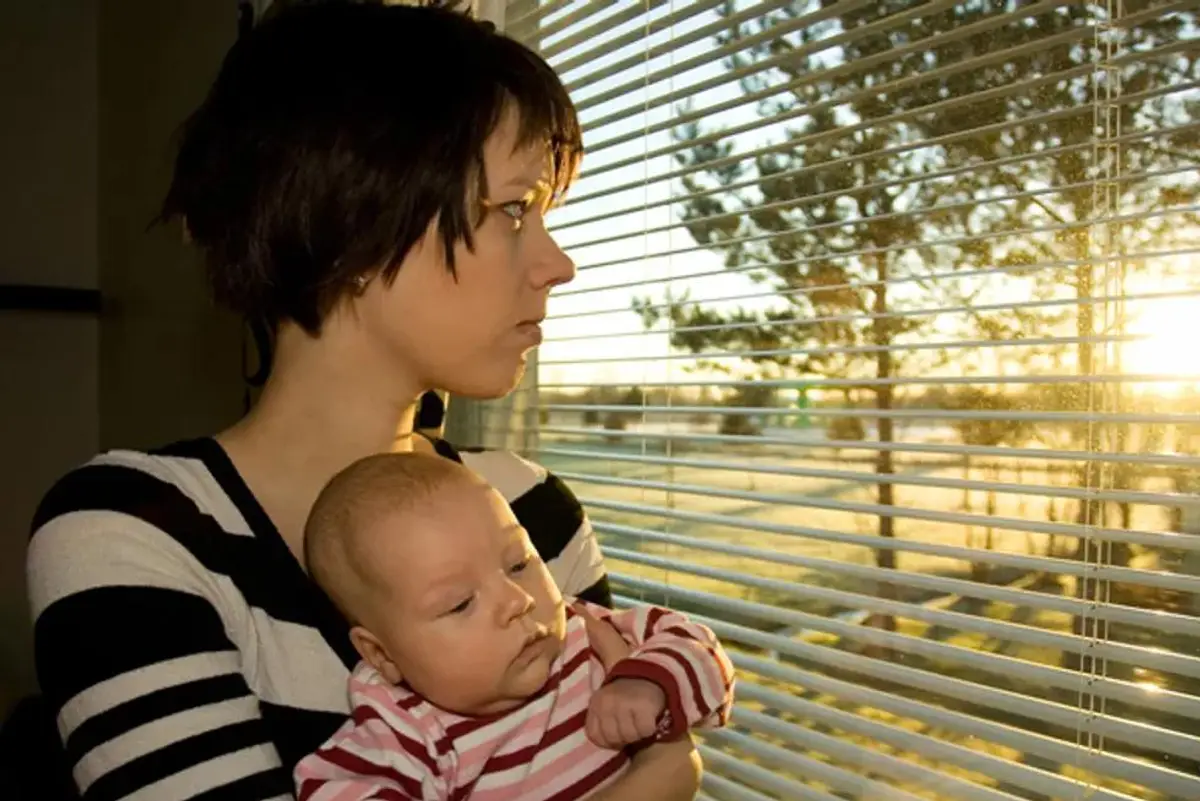 sad woman holding a baby looking out a window