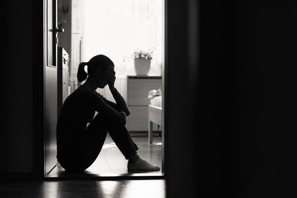 Sad young woman sitting on a floor at home