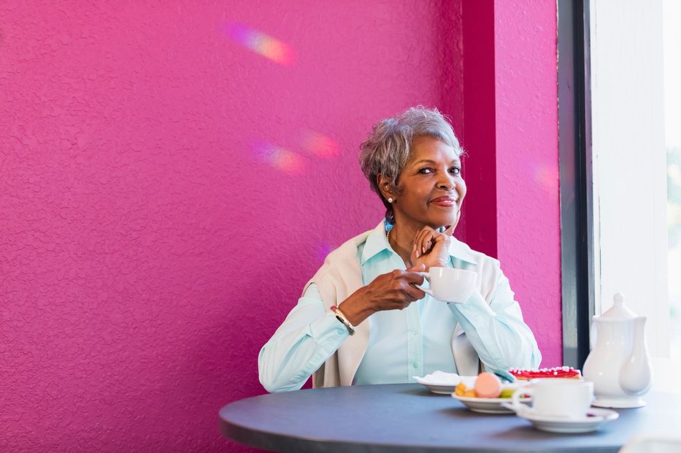 senior African-American woman in her 70s sitting at a table in a coffee shop, having coffee and pastries