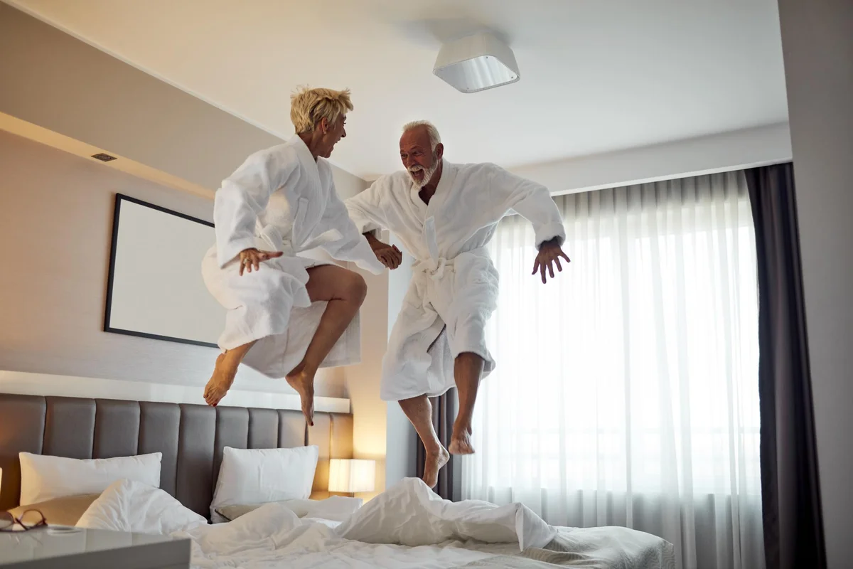 Senior couple jumping on the bed and having fun in hotel room