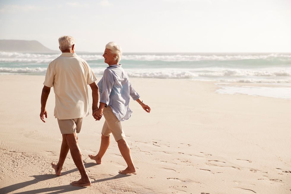 Senior Couple Walking Along Beach Hand In Hand