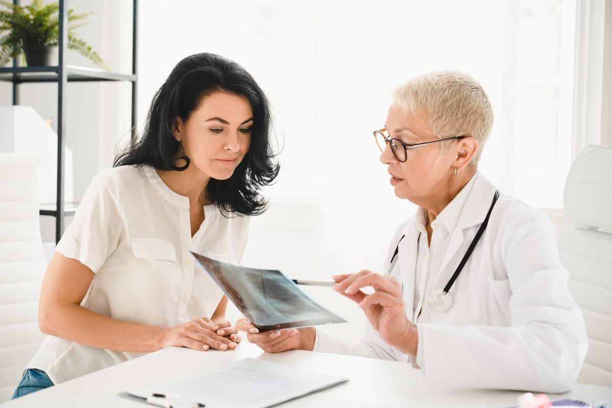 senior female doctor general practitioner showing x-ray lungs photo to female patient, explaining diagnosis