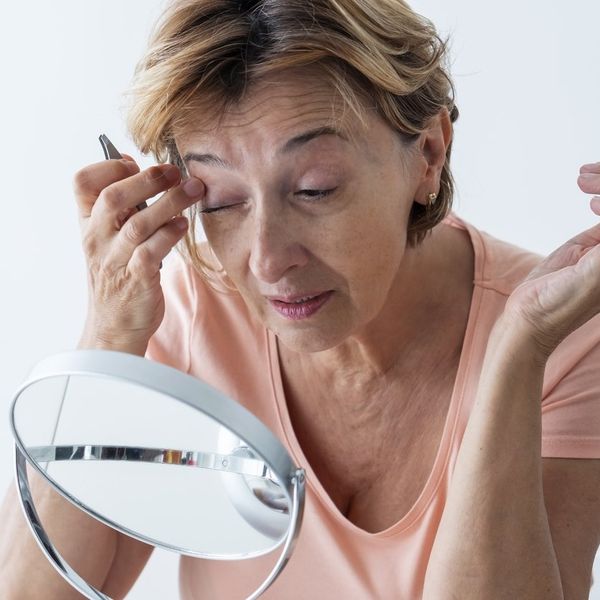 Senior woman shaping her eyebrows with tweezer at home.