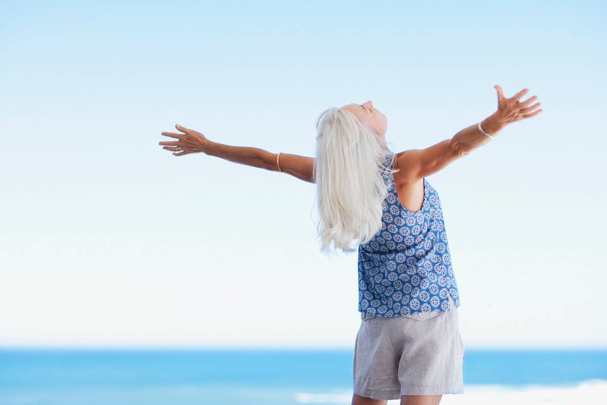 Senior woman standing with arms outstretched on beach