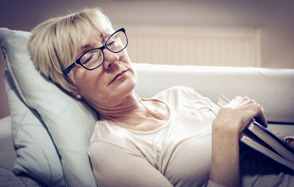 Senior woman suffering from sleep apnea, sleeping on the couch and holding book