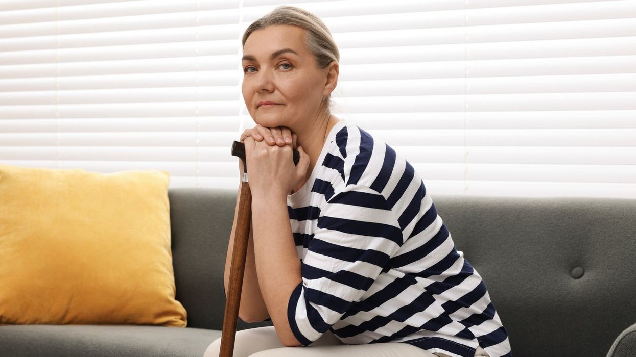 Senior woman with walking cane sitting on sofa at home