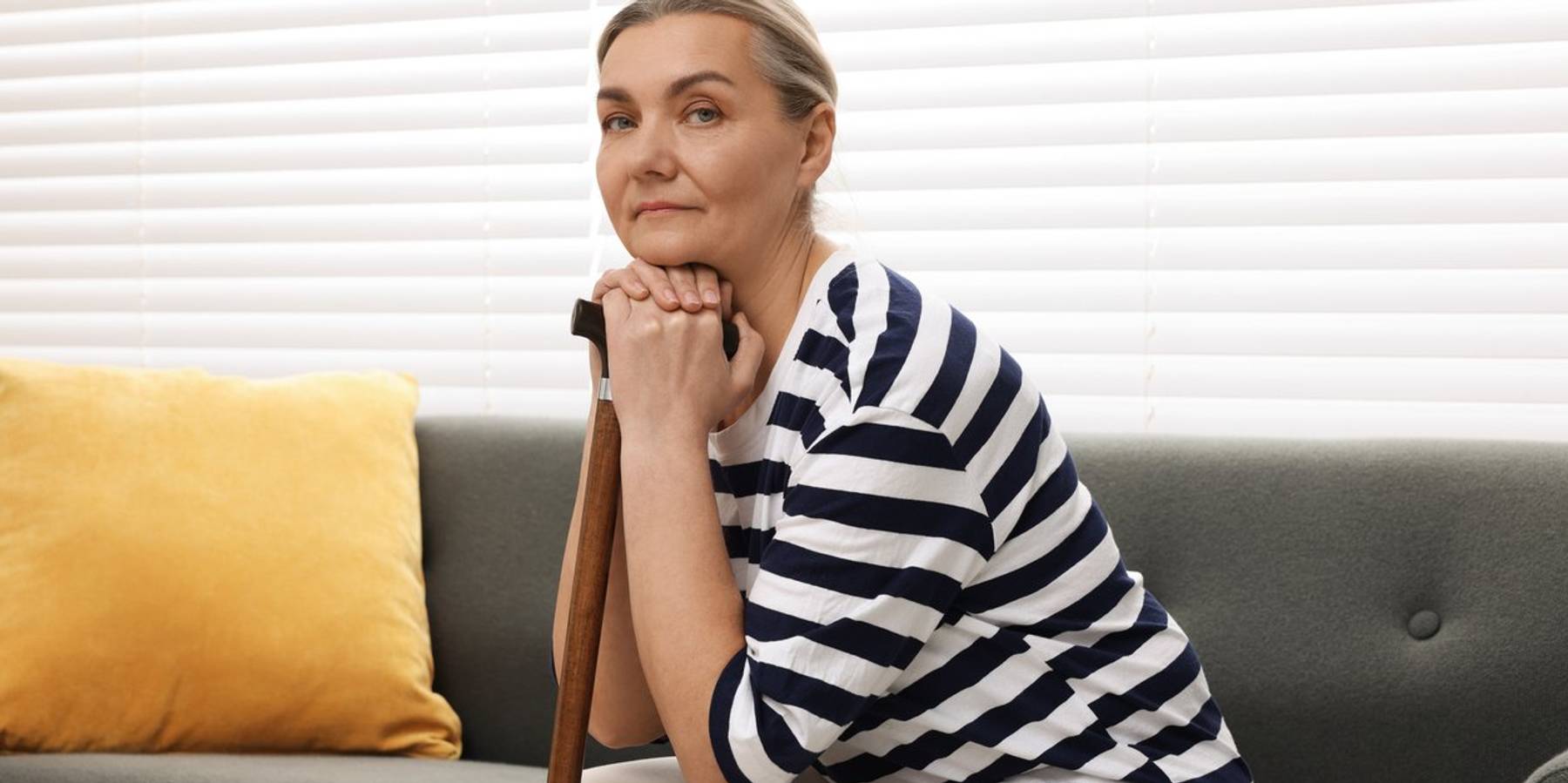 Senior woman with walking cane sitting on sofa at home