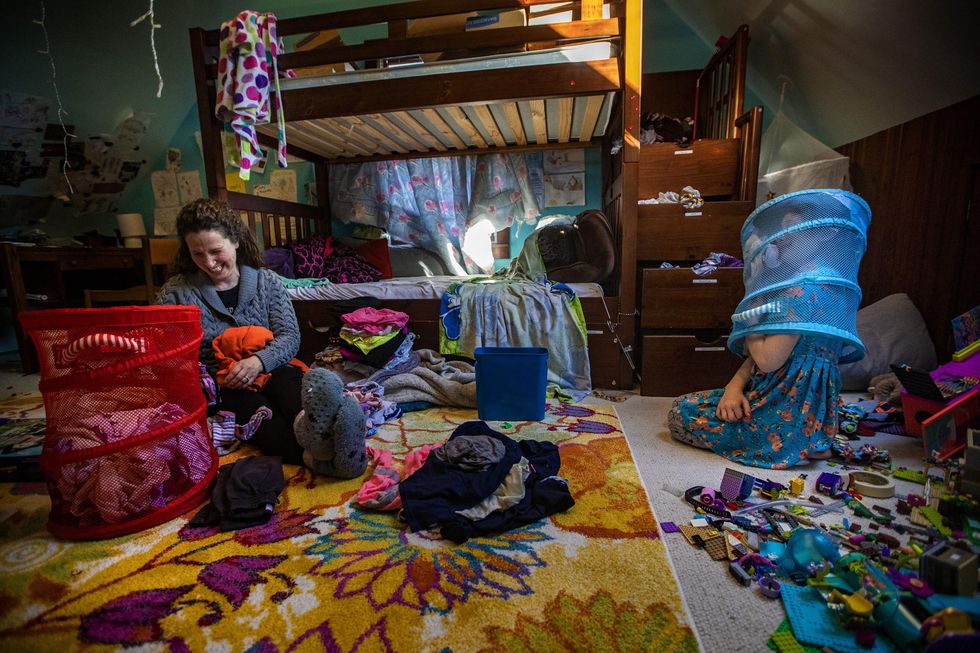 Shira laughs as Hallel places a laundry basket on their head.