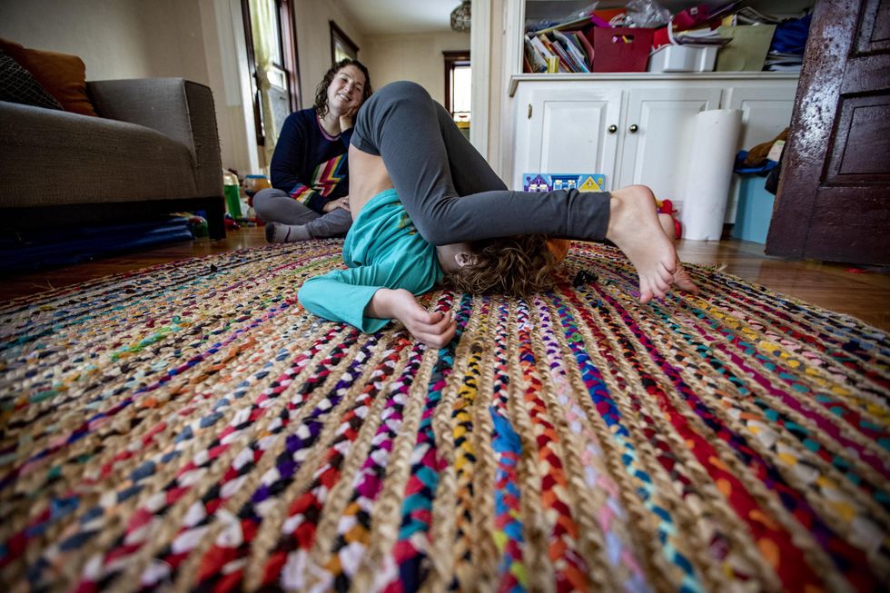 Shira watches as Hallel does a backwards roll in the living room.