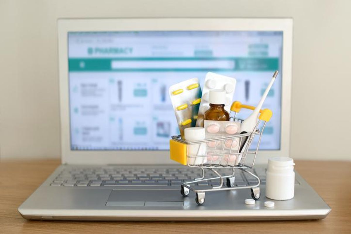 Shopping cart toy with medicaments in front of laptop screen with pharmacy web site on it.