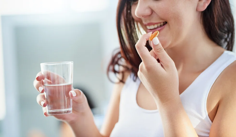 Shot of a young woman taking a pill with a glass of water during her morning routine at home