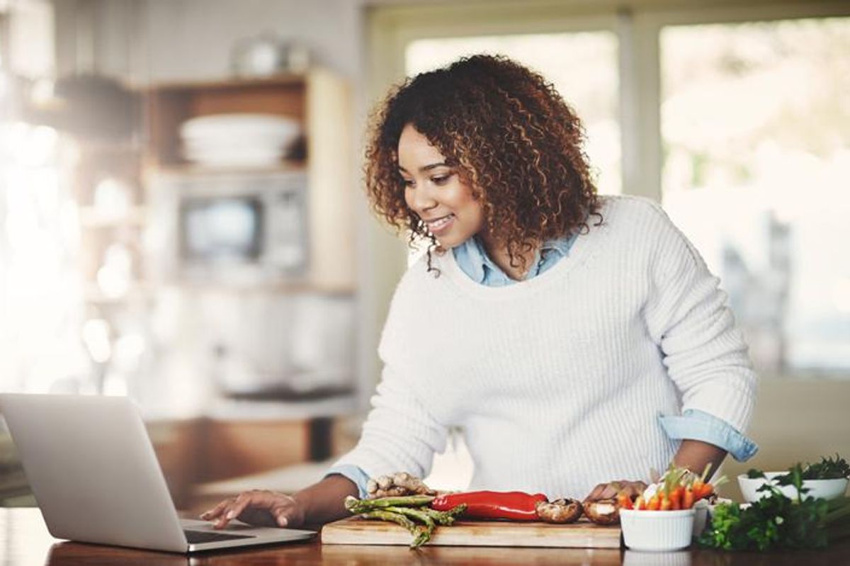 Shot of a young woman using a laptop while preparing a healthy meal at home